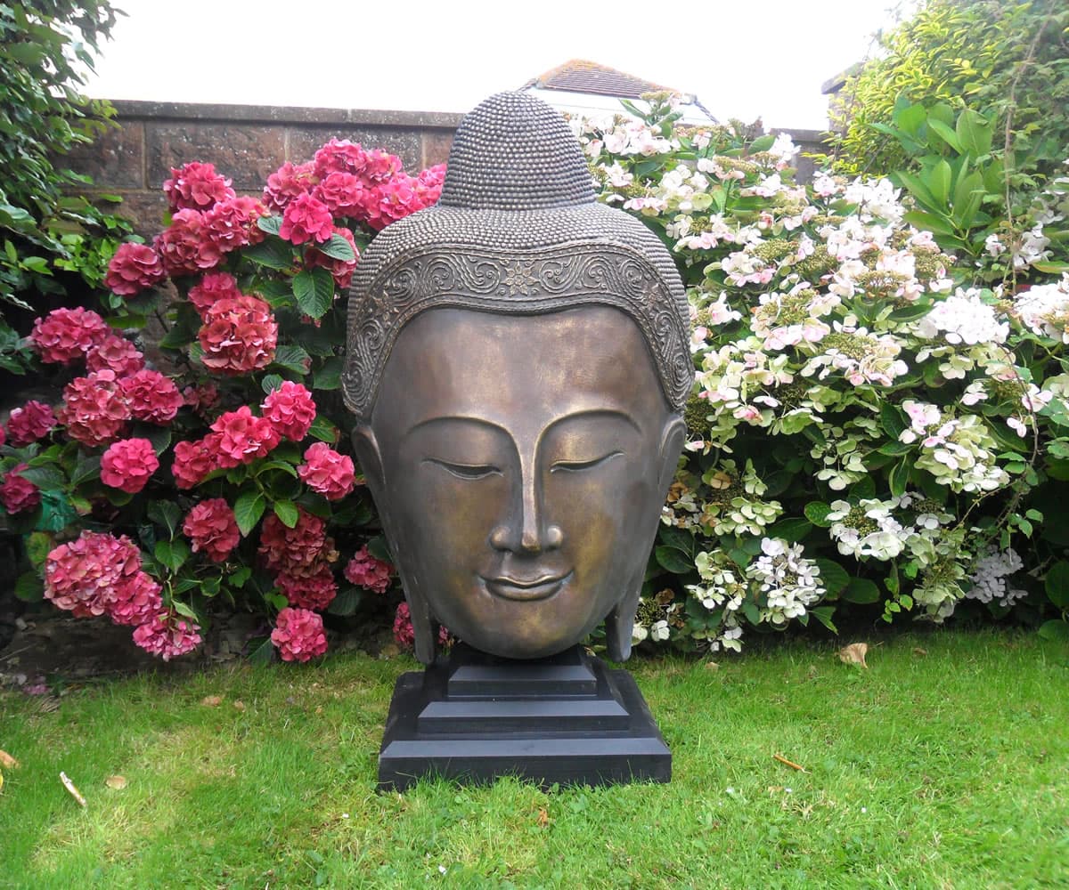 A bronze Buddha garden statue surrounded by flowering shrubs
